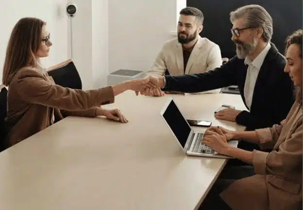 Four people sitting at meeting table - two people are shaking hands.