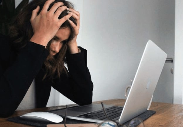 Woman with hands on head in frustration with work-life balance looking at computer