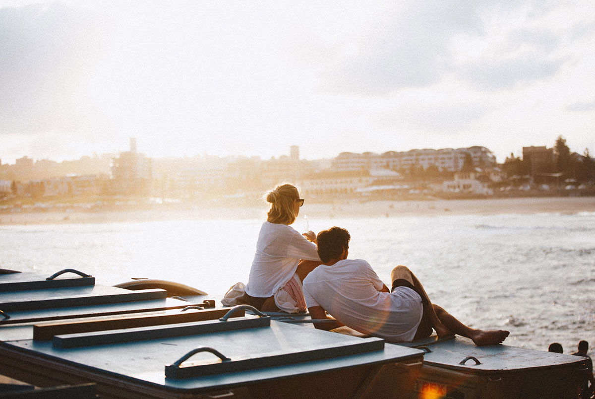 Man and woman sitting on pier looking out over the ocean at sunset