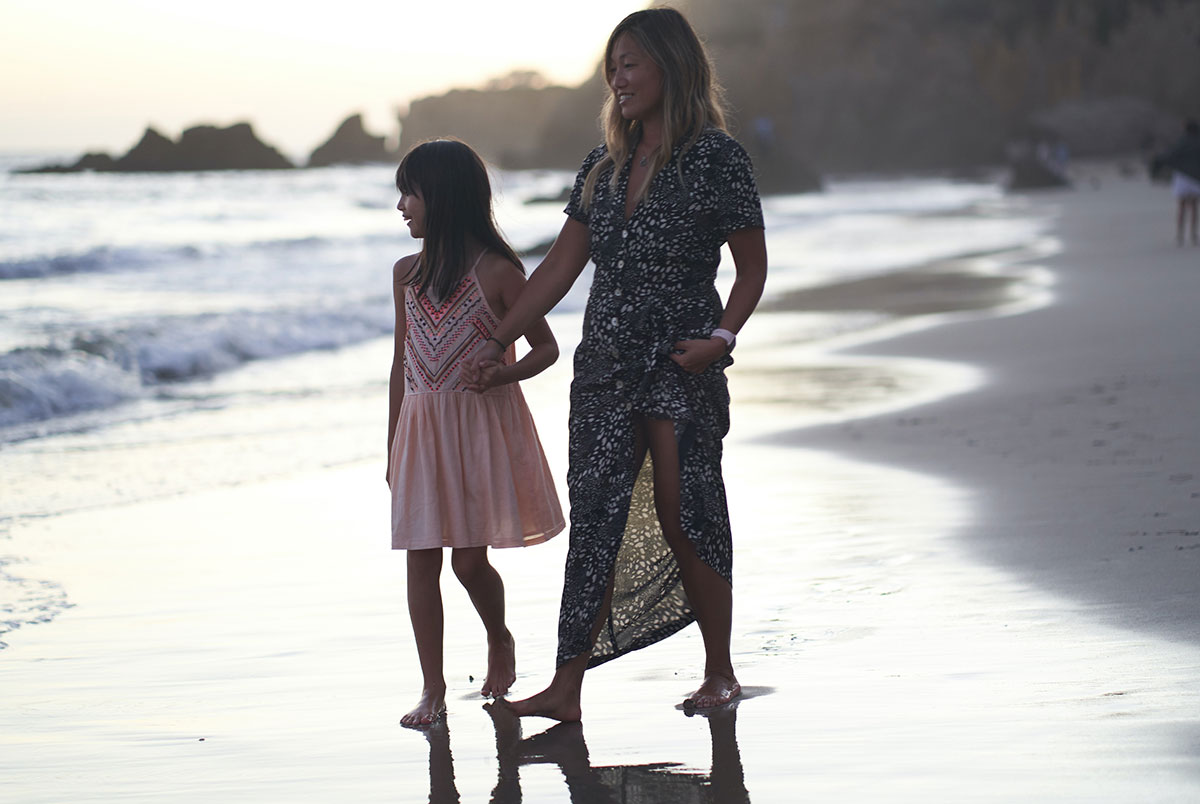 Woman and child walking on the beach barefoot at sunset