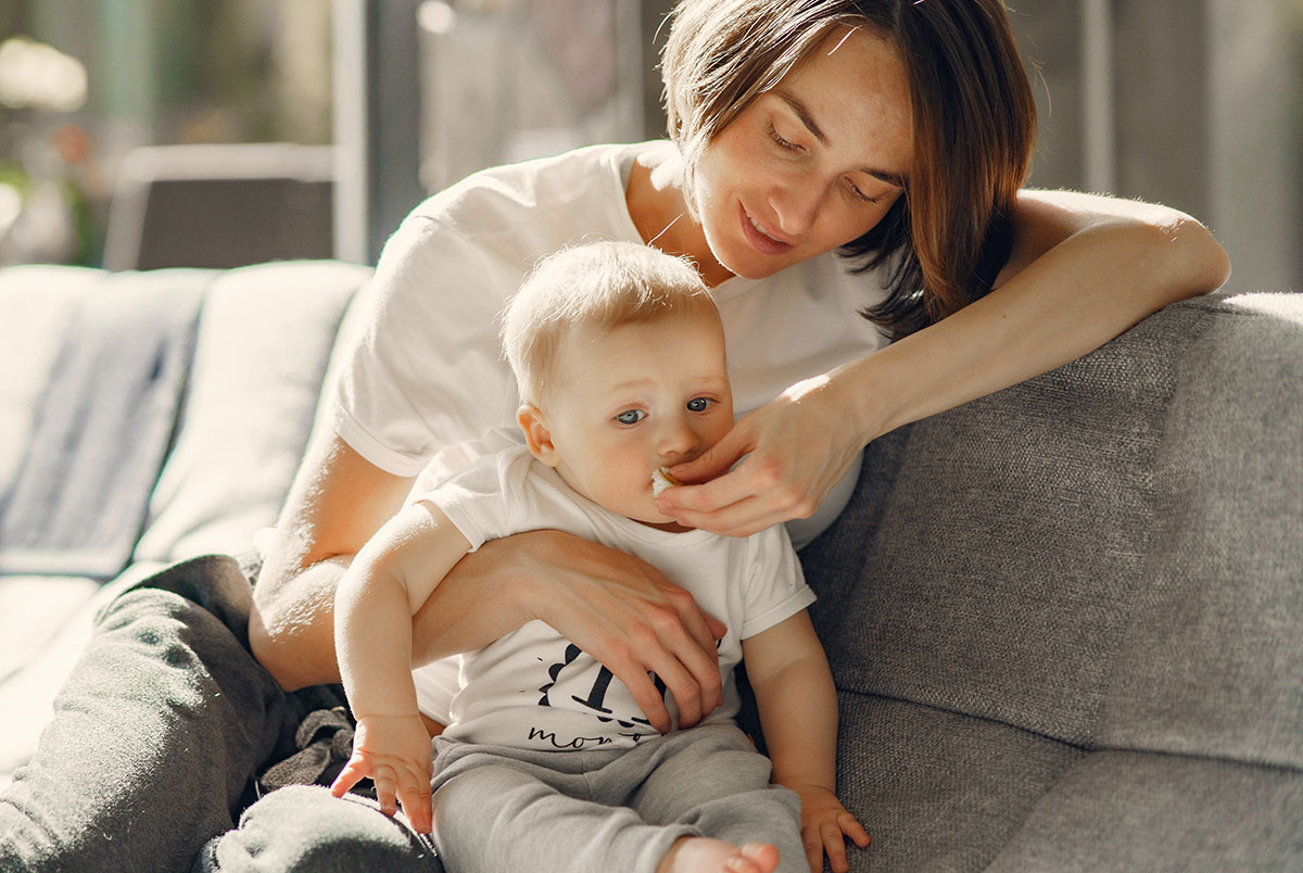 Woman helping feed baby while sitting on the couch