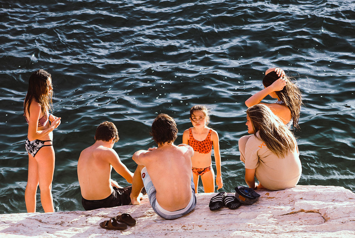 Group of children sitting and standing on concrete steps next to the ocean