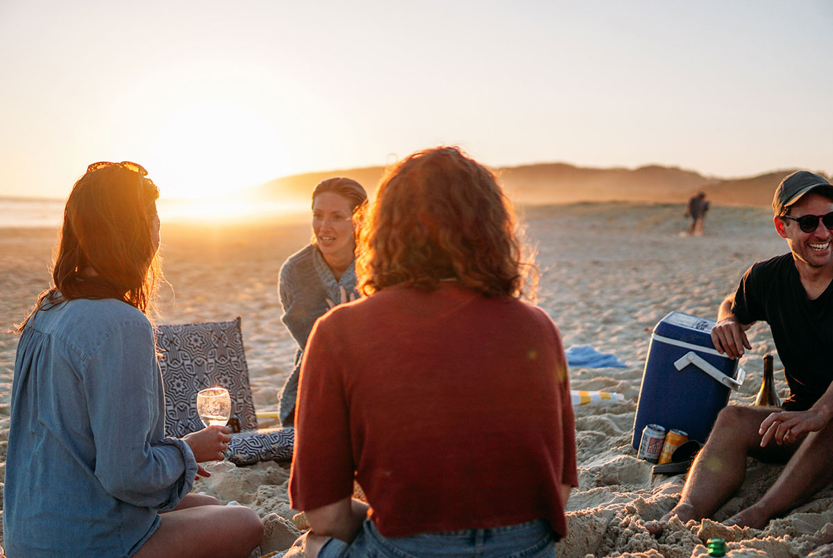 Group of people sitting in a circle on the sand at sunset, displaying a relaxed and enjoyable gathering without any signs of social awkwardness.