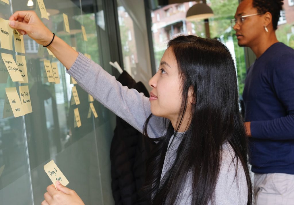 Person sticking a post it note up on a board.