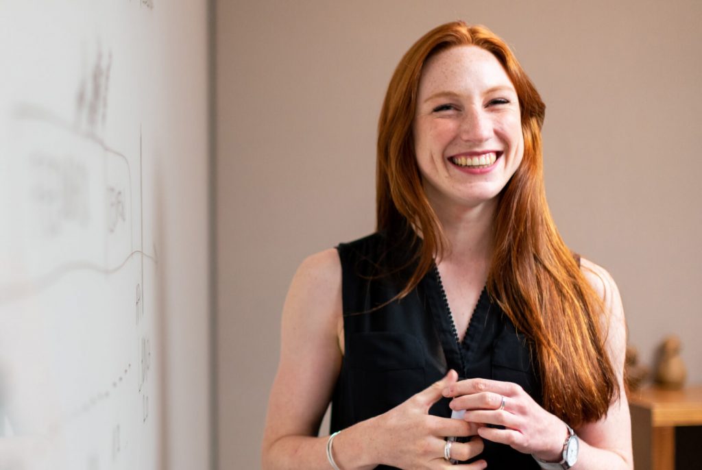 Girl standing beside white board smiling.