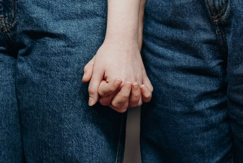 Two people wearing blue jeans holding hands.