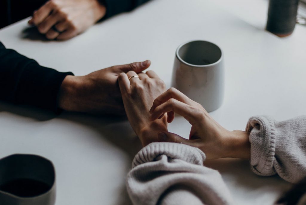 Two people holding hands over a table with a coffee mug.