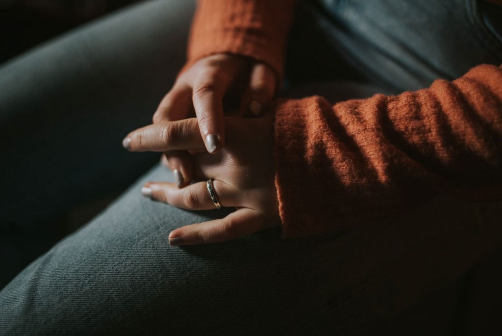 A person wearing an orange sweater holding their hands in their lap.