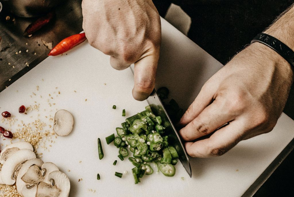 A person slicing a chilli on a white chopping board.