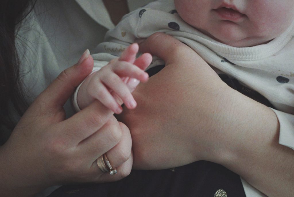 A baby holding the index finger of an adult.
