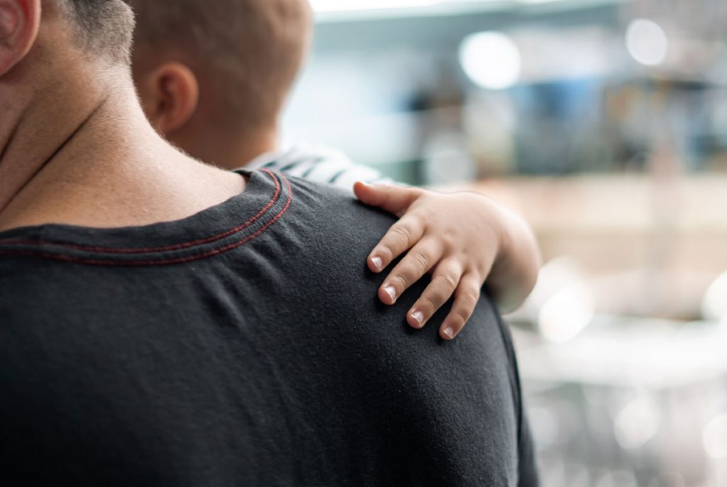 A baby's hand reaching around a person's shoulder.