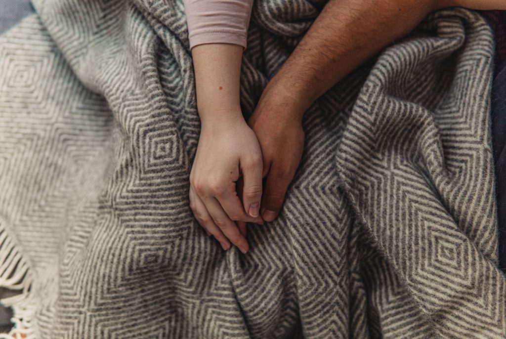 Two people holding hands on a blanket.