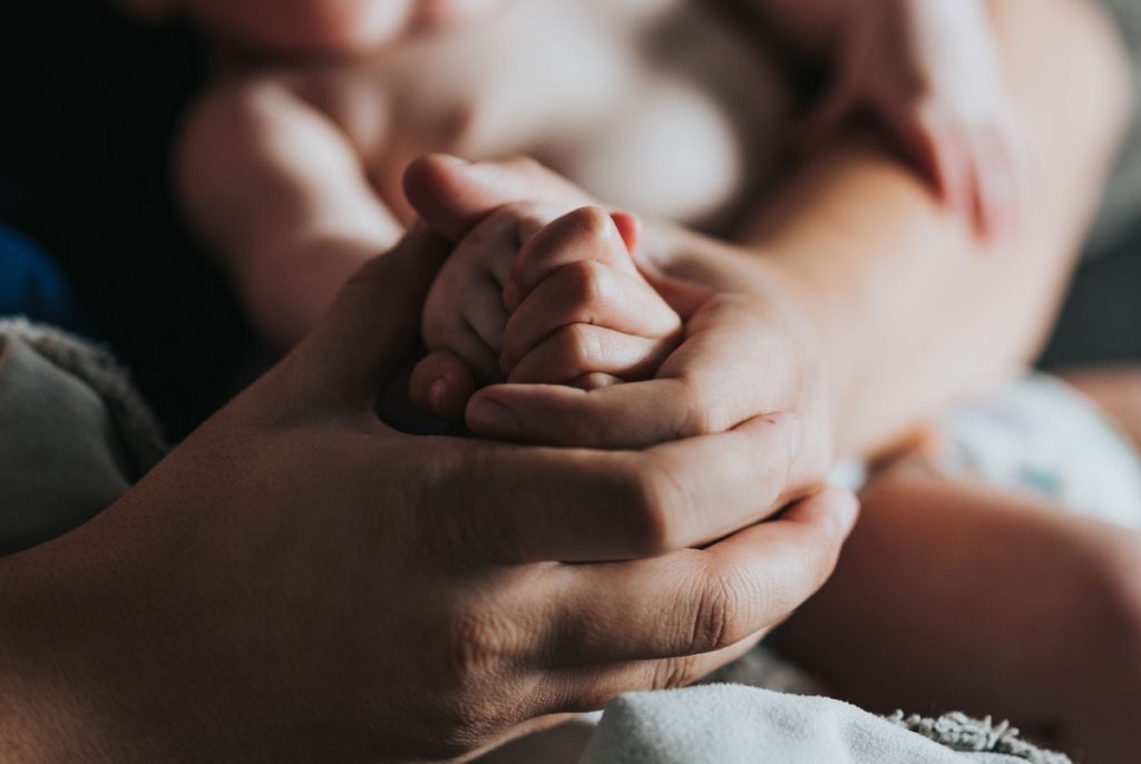 A baby's hands cupped between an adult's hands.