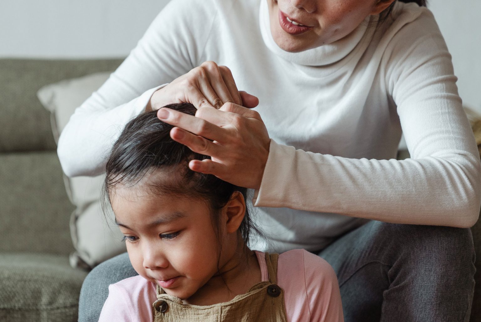 Mother sitting on couch smoothing the hair of child sitting on the floor, nurturing resilient kids