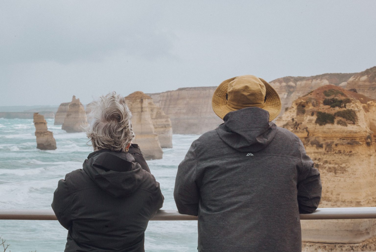 Man and woman wearing rain jackets leaning on railing looking out at the 12 apostles