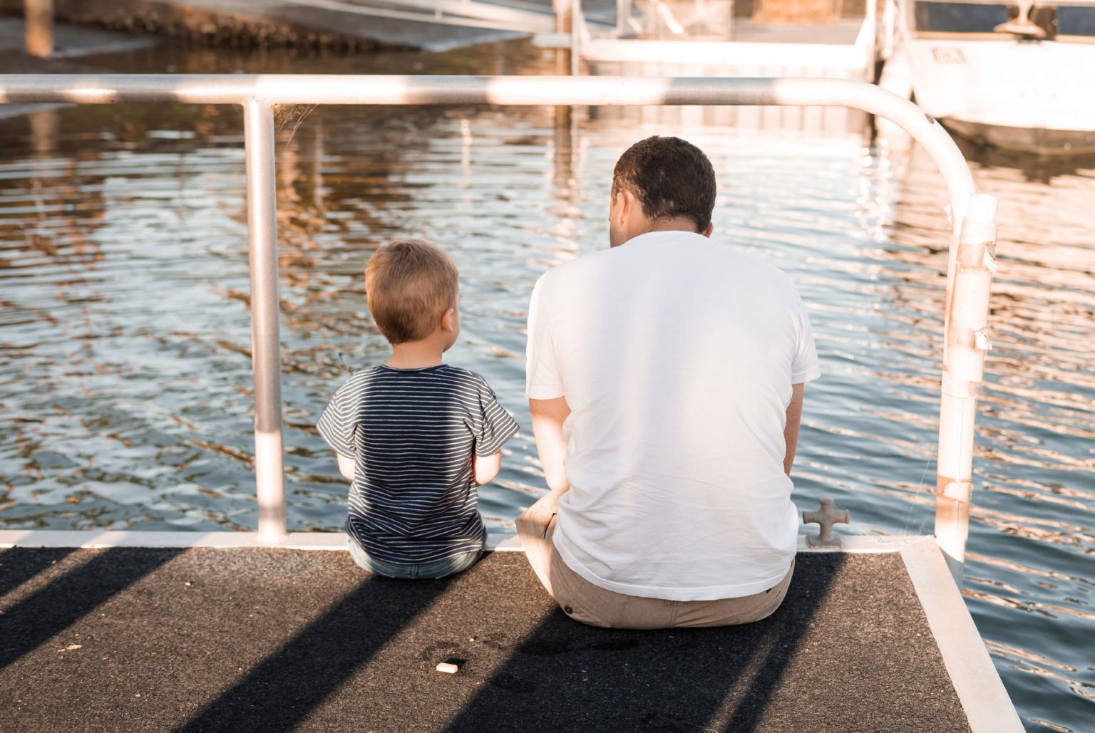 Man and boy sitting on a jetty over the water