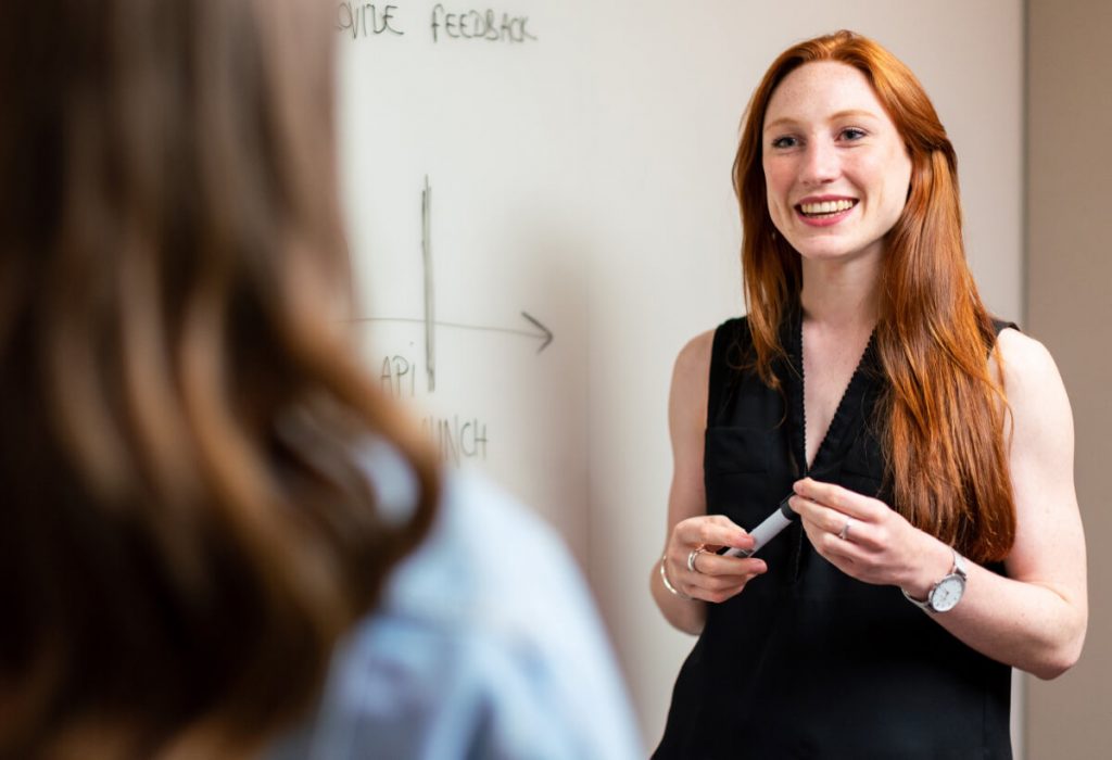 Woman standing beside white board talking to someone.