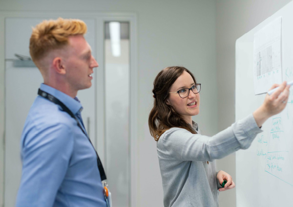 Woman pointing out something on a white board to a man.