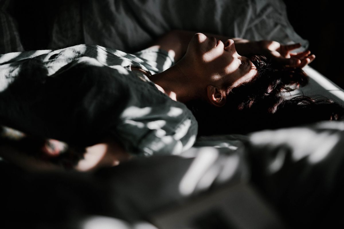 Woman lying on the bed on her back with shadow of blinds on her face