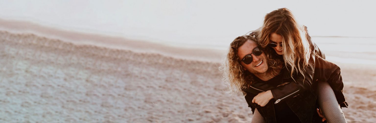 Girl piggy backing a man on the sand at sunset