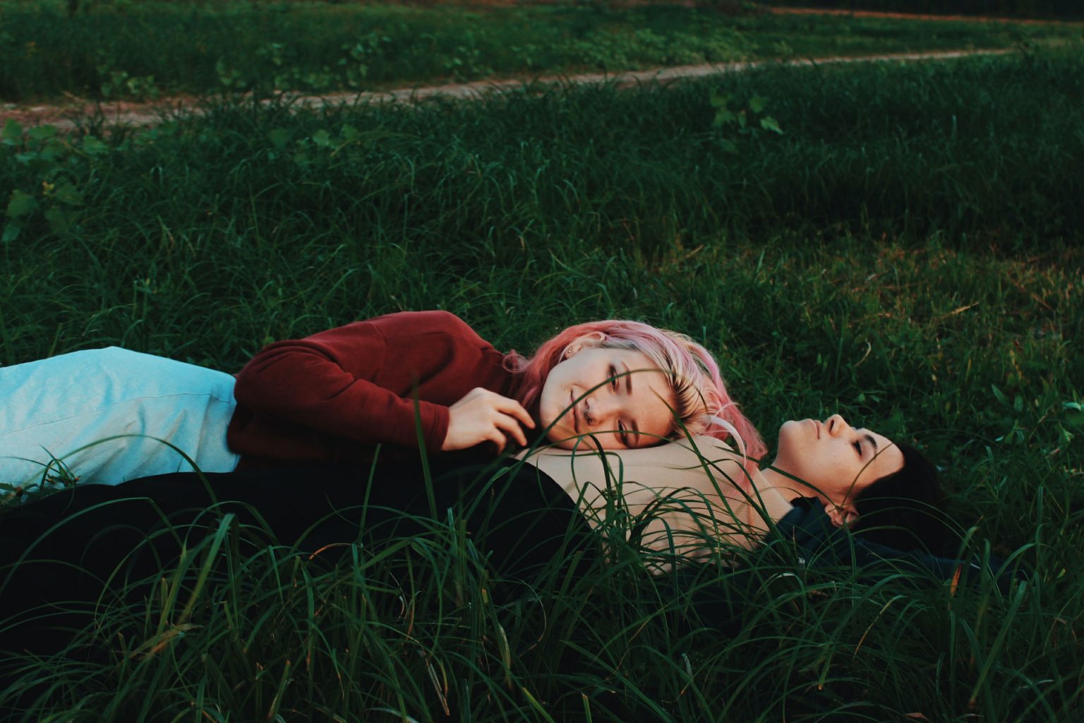 Two women lying in grass one with her head resting on the chest of the other, smiling