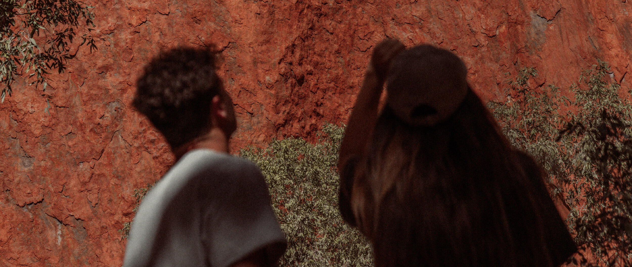 Two people staring up at red rock face.