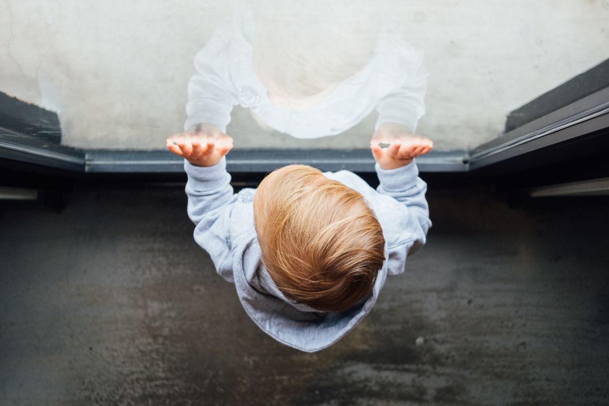 Young child standing with hands against the window looking outside