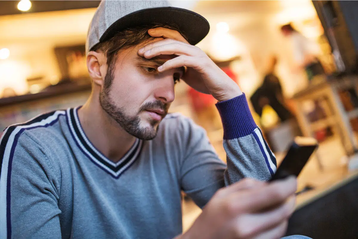 Man in baseball cap worried and ruminating looking at his phone