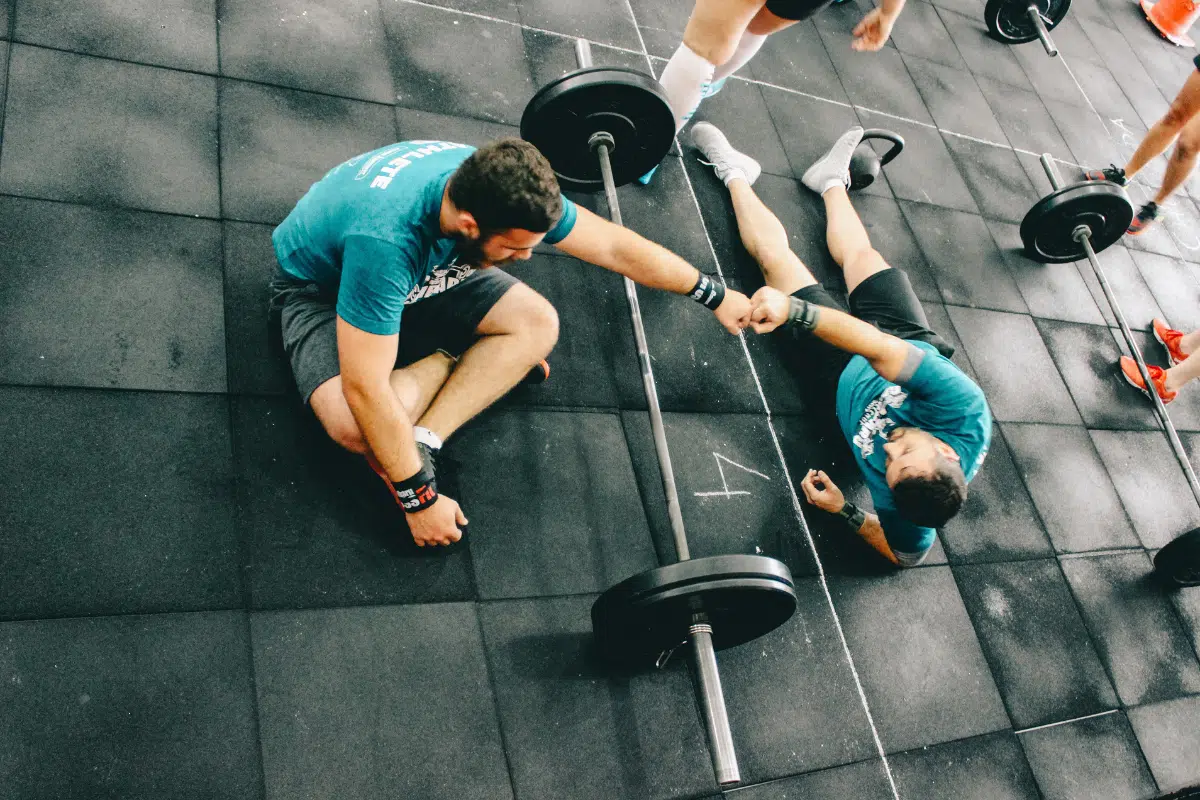 Two men in gym using weights, fist-bumping.