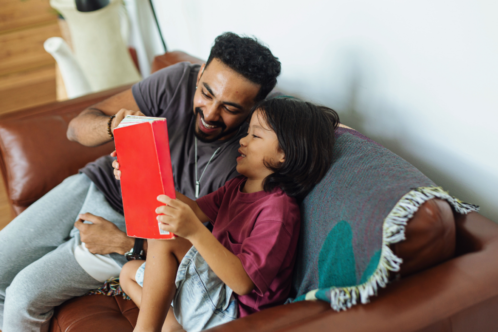 A man and a child sitting side by side, immersed in reading a book together