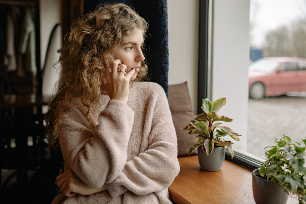 Young woman holding phone to ear and looking out window.