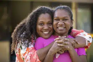 Two young aboriginal female students outdoors with their arms around each other smiling at the camera.