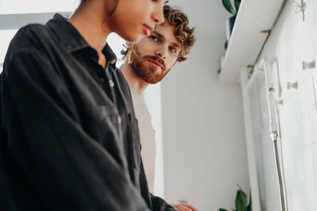 man standing beside female partner looking at her in kitchen