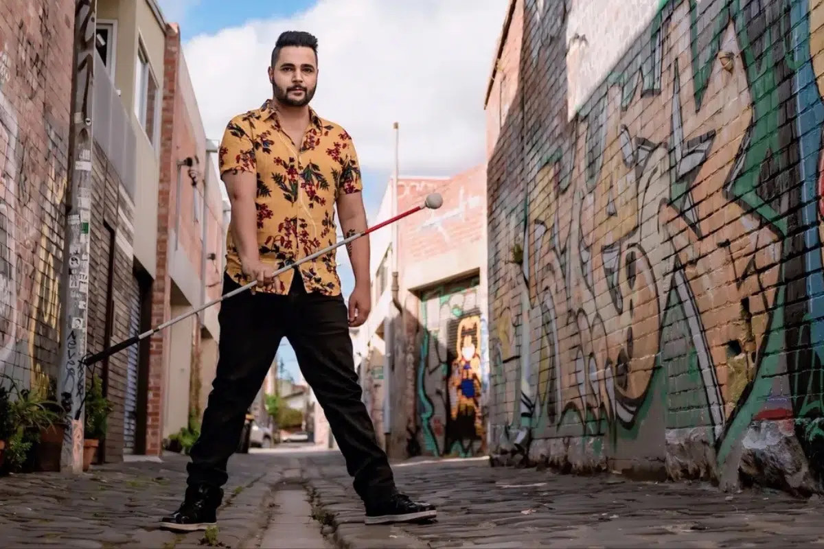 Karan Nagrani standing in a graffitied laneway holding his cane